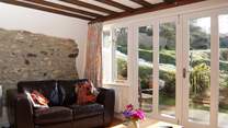 The sun pours into the living-area. There are two arm chairs as well as the sofa.
