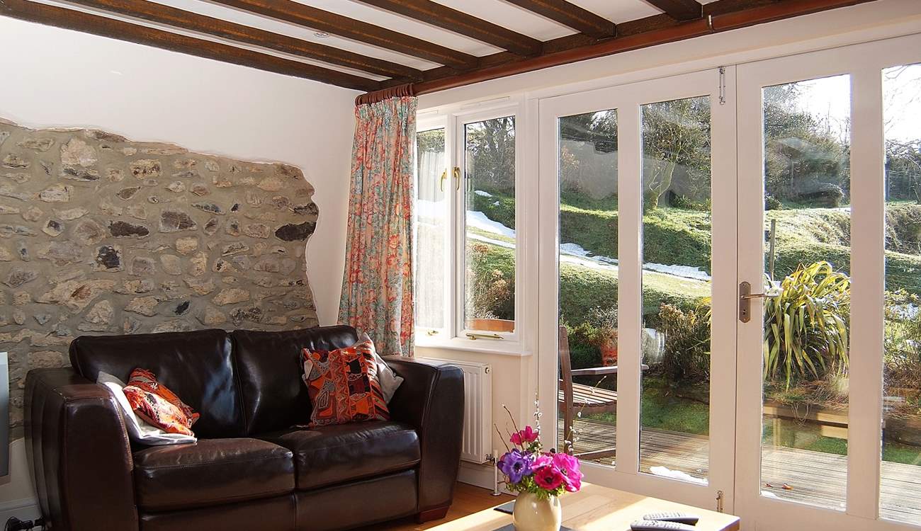 The sun pours into the living-area. There are two arm chairs as well as the sofa.