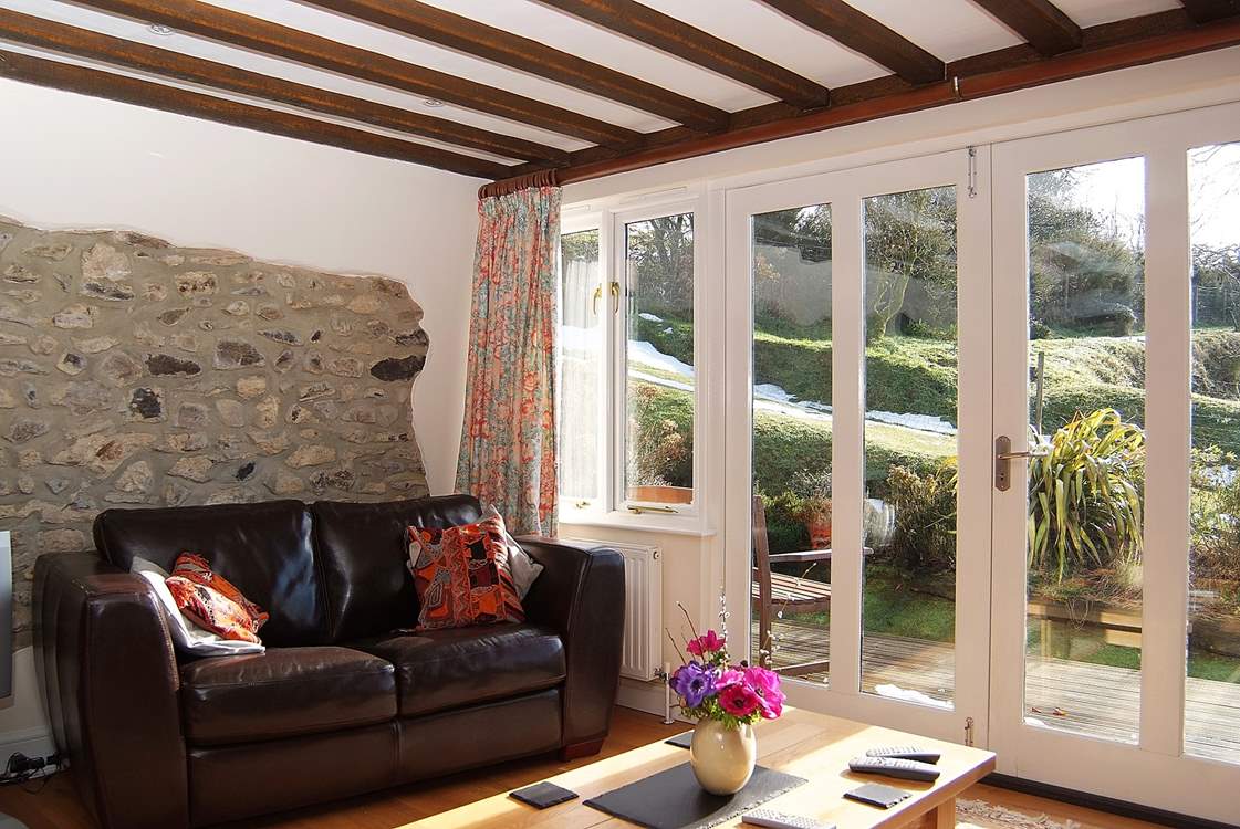 The sun pours into the living-area. There are two arm chairs as well as the sofa.