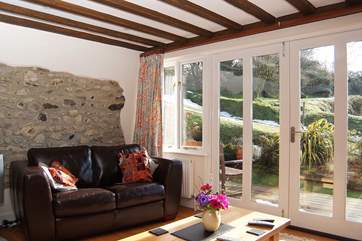 The sun pours into the living-area. There are two arm chairs as well as the sofa.