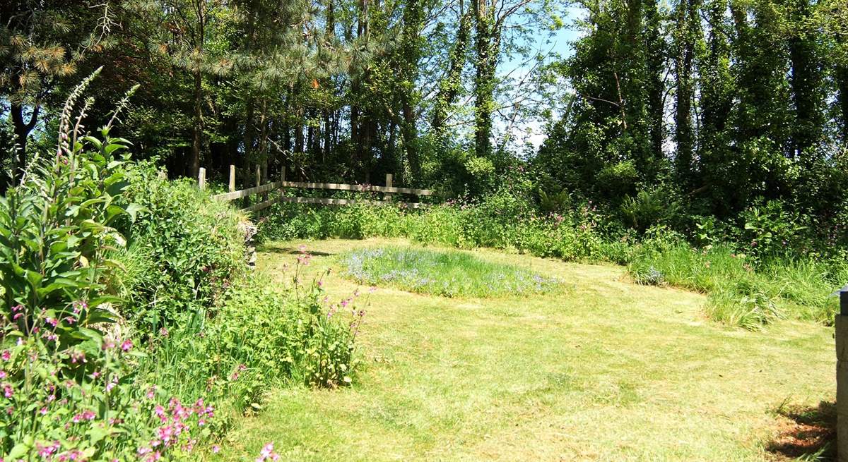 The lawn behind the cottage slopes up towards the surrounding trees.