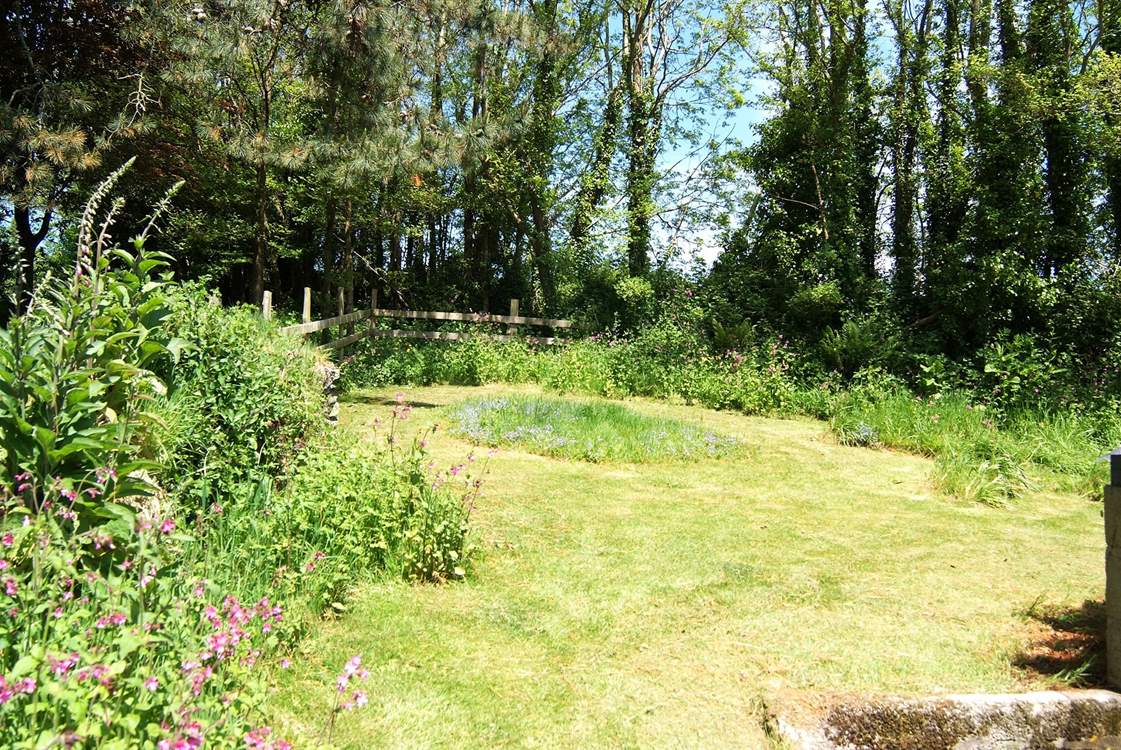 The lawn behind the cottage slopes up towards the surrounding trees.