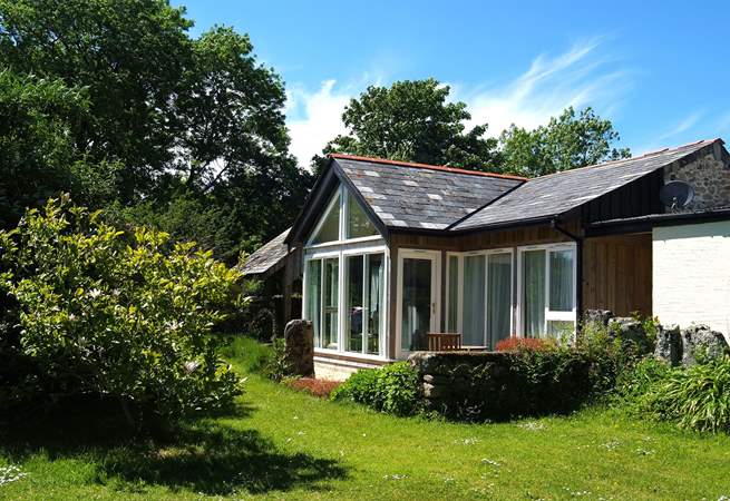 The timber-framed glass wall of the south-facing open plan living-room in Snuggledown, gives views over the fields and woods of Trevethey Farm.