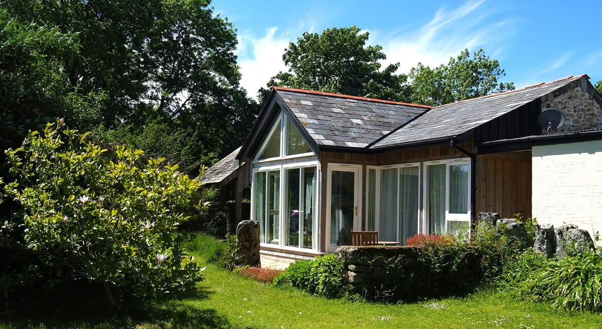 The timber-framed glass wall of the south-facing open plan living-room in Snuggledown, gives views over the fields and woods of Trevethey Farm.