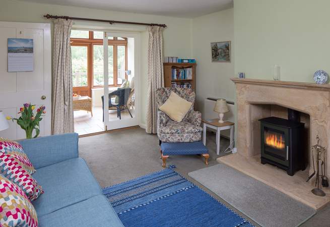 The open plan sitting/dining-room has a beautiful hamstone fireplace, cosy wood-burner and the garden-room beyond.