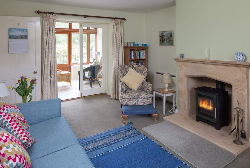 The open plan sitting/dining-room has a beautiful hamstone fireplace, cosy wood-burner and the garden-room beyond.