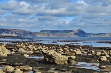 Low tide in Lyme Regis on the Jurassic Coast, with a view of Golden Cap - the Dorset coast's highest point in the distance. Have a great day out with breathtaking walks and a spot of fossil hunting!