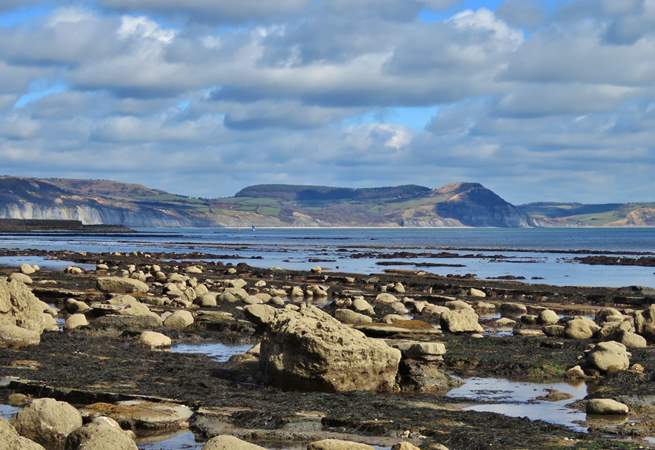 Low tide in Lyme Regis on the Jurassic Coast, with a view of Golden Cap - the Dorset coast's highest point in the distance.  Have a great day out with breathtaking walks and a spot of fossil hunting!