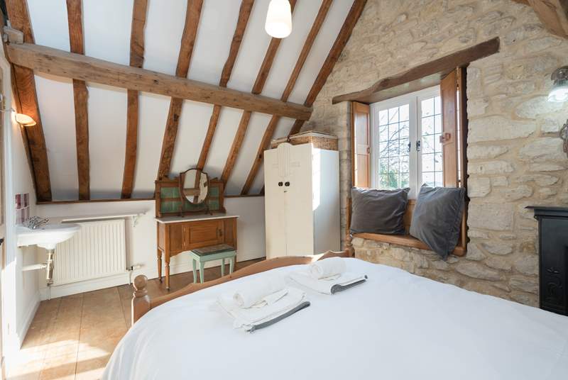 The bedroom has lovely exposed stone walls and a tall beamed ceiling.