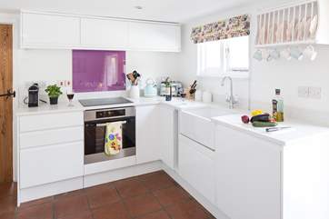 The crisp white kitchen has an induction hob, butler sink, fitted dishwasher and is fully equipped to create a delicious meal.