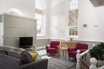 The sitting-area in the open plan living-room has tall arched windows and a high apex ceiling.