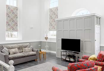 The sitting-area in the open plan living-room has tall arched windows and a high apex ceiling.