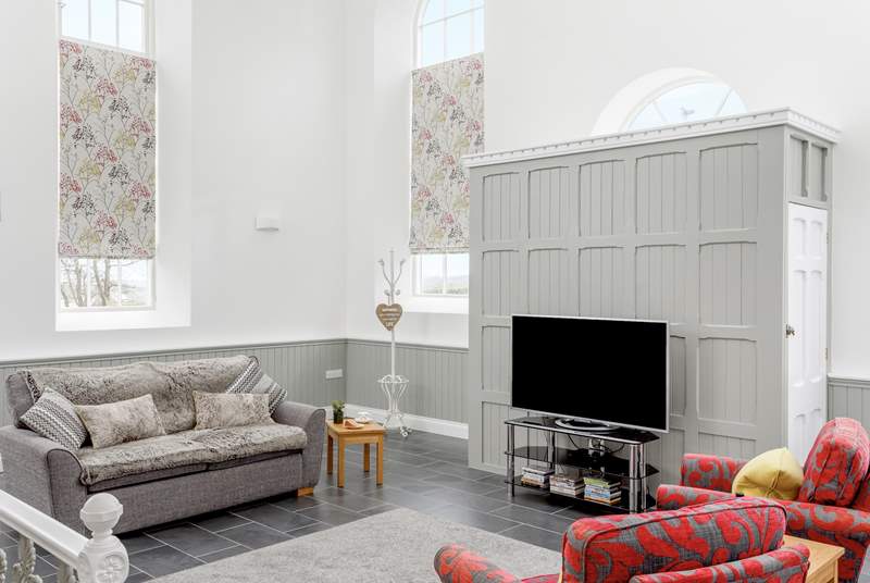The sitting-area in the open plan living-room has tall arched windows and a high apex ceiling.