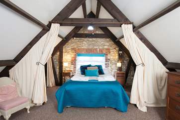 The master bedroom has sloping ceilings with revealed beams, feature stonework and dressing-area with seating.