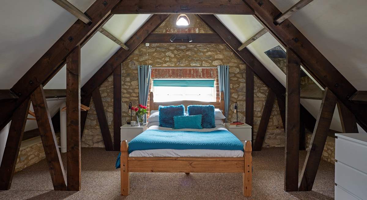 The master bedroom has sloping ceilings with revealed beams, feature stonework and dressing-area.