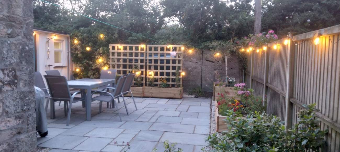 The patio at dusk - pretty lights and colourful flower beds.