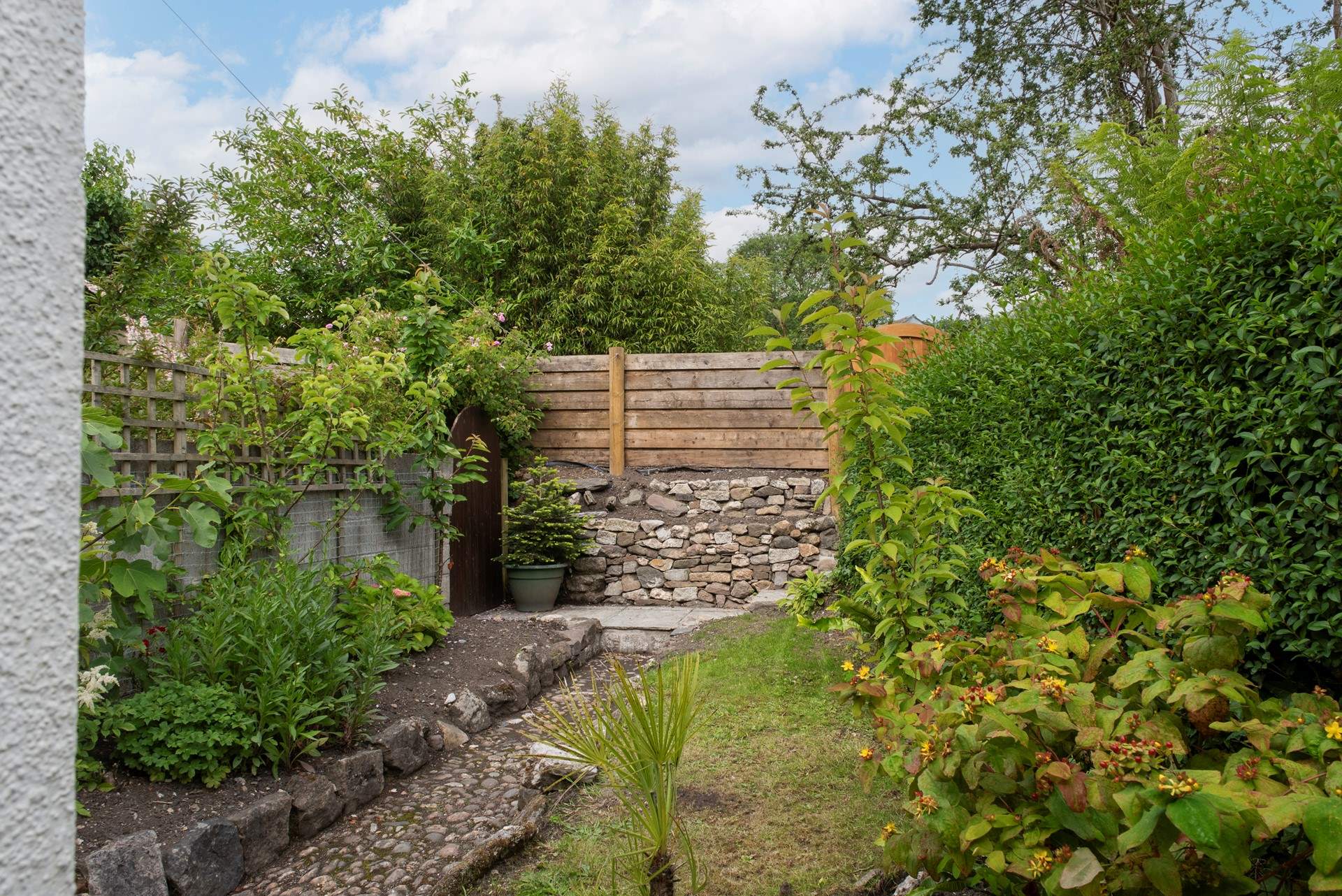 The rear garden area is a tranquil space filled with greenery. A gate leads out to a footpath which takes you down to the harbour.