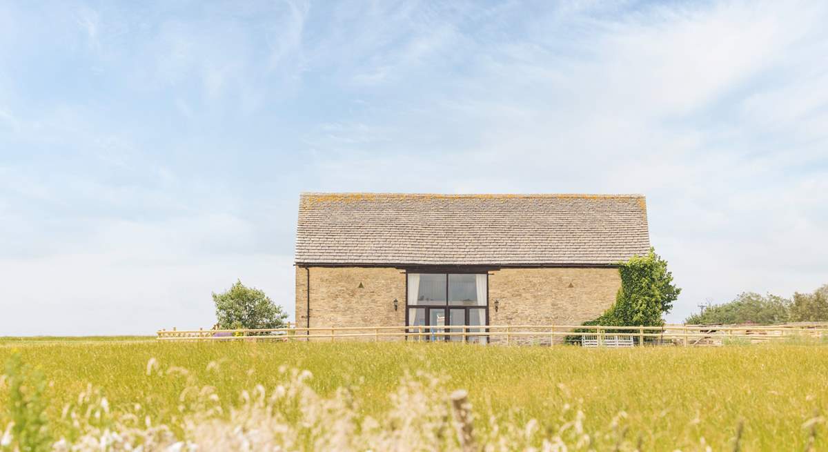 The barn appears at the end of a track, off a quiet country lane, rising slightly above the surrounding fields