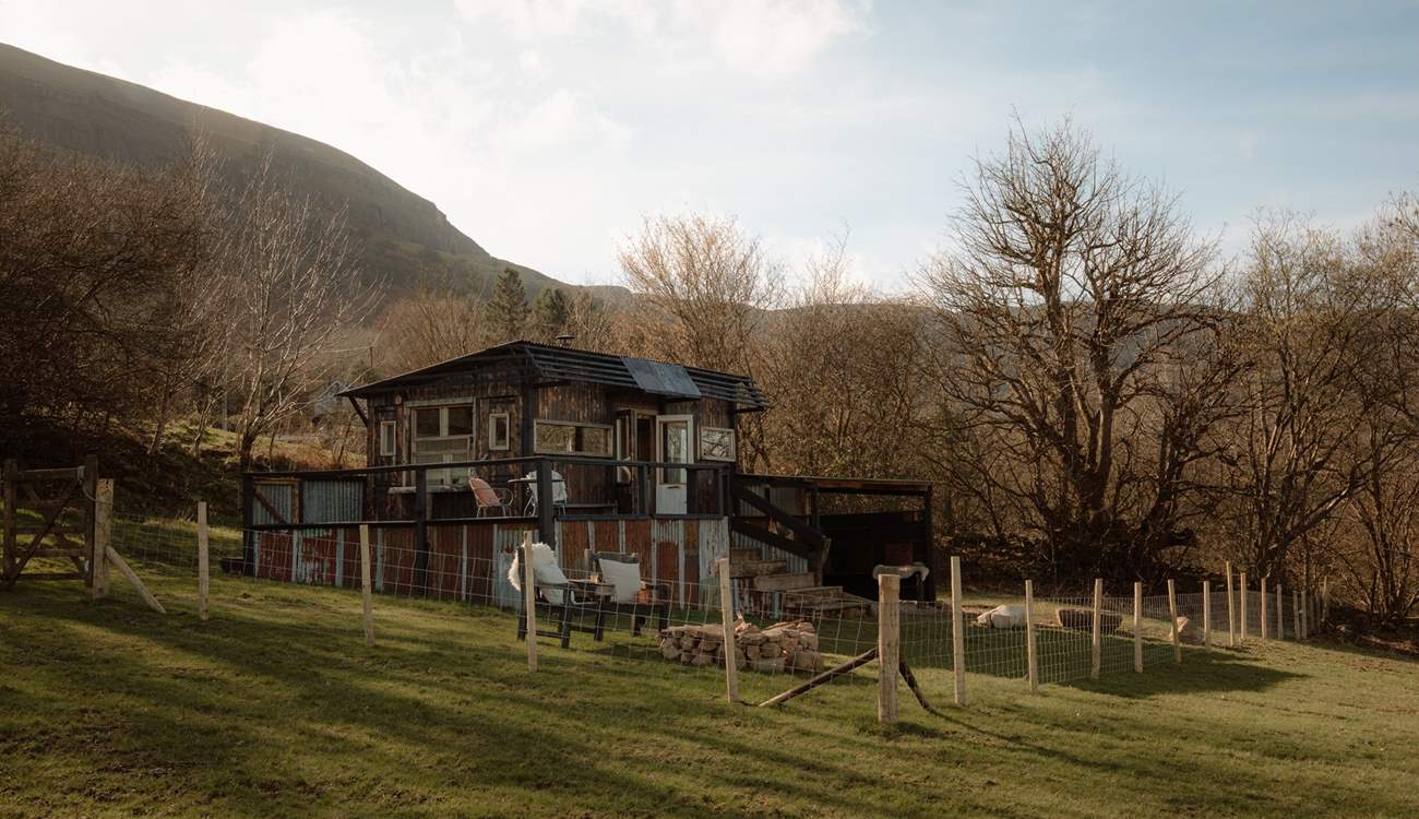 The cabin sits within its own enclosed garden, where wide views stretch across patchwork countryside to distant peaks.