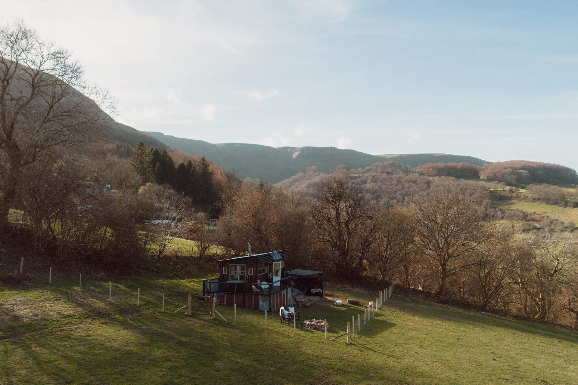 The cabin sits within its own enclosed garden, where wide views stretch across patchwork countryside to distant peaks.