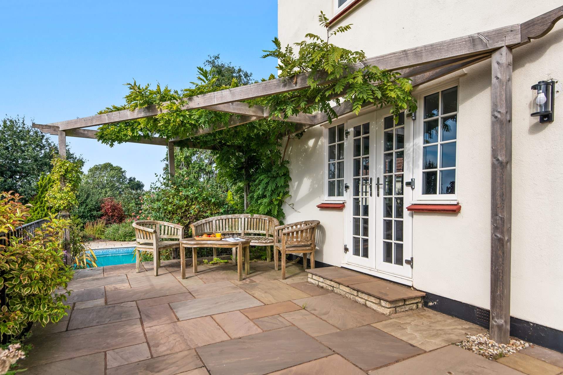 Step out of the sun-room onto the patio, where another beautiful seating-area awaits. This spot enjoys the laughter and splashes from the swimming pool beyond.