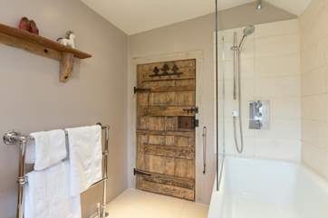 There is a contemporary family bathroom with a bath and fitted shower. The historic door balances perfectly with the sparkling white fittings.