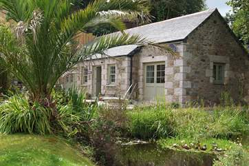 The front of this luxurious property next to a pond with a terrace and steps to the left which run up to a wonderful second decked terrace.