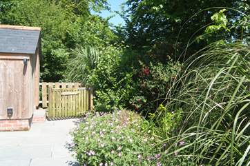 The pretty patio garden is surrounded by shrubs with the gate open onto the coast path.