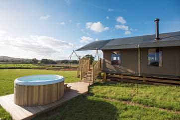 The hot tub sits proud on its own deck to the side of the tent.